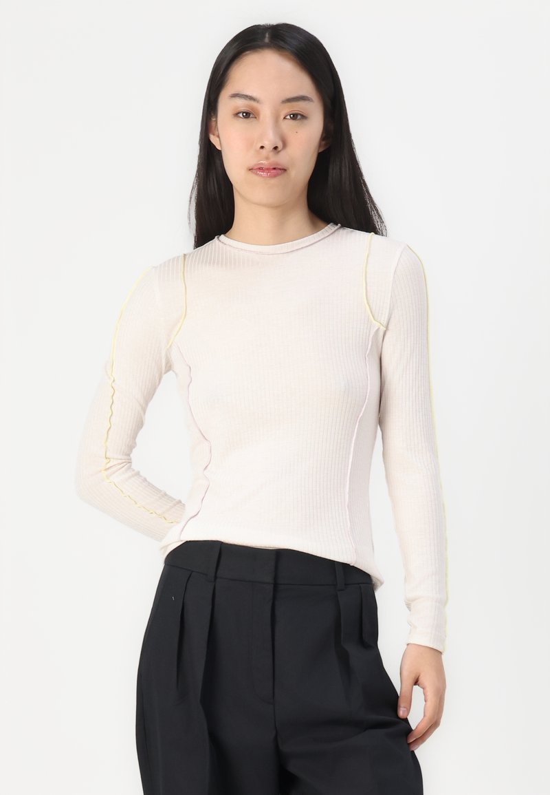 Gestreiftes Langarmshirt in hellbeige mit kontrastierenden gelben und pinken Nähten, runder Ausschnitt und taillierte Silhouette.