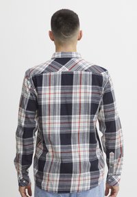 Camisa de franela a cuadros en azul marino, blanco y rojo. Cuenta con mangas largas, puños con botones y un collar clásico con un corte regular.