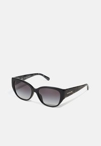 Schwarze Sonnenbrille mit einer markanten Cat-Eye-Form, verlaufenden Gläsern und strukturierten, grau akzentuierten Bügeln mit einem goldenen Logo-Detail.