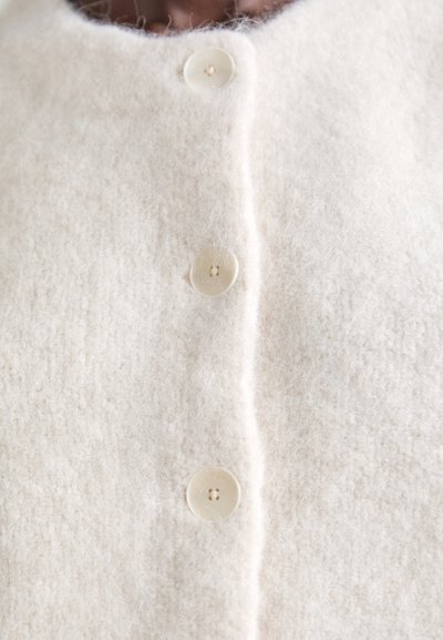 Cardigan di lana color crema con una finitura morbida e testurizzata e quattro bottoni rotondi color crema sulla parte anteriore.