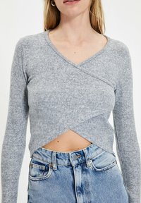 Grå, langærmet cropped sweater med indviklet design, lavet af blødt materiale. Har en dyb V-hals og rundet kant over taljen.