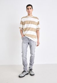 Randig oversized t-shirt i beige och vitt med en bröstficka, i kombination med ljusgrå slim-fit jeans och grå skor med svarta snören.