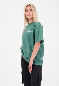 Groen oversized T-shirt van katoen met een vervaagde wassing. Heeft een ronde halslijn en een wit tekstlogo gedrukt op de voorkant.