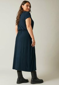 Sukienka w kolorze granatowym o długości średniej, z marszczonym pasem i krótkimi rękawami, zestawiona z czarnymi botkami na kostkę. Gładki materiał o minimalnej teksturze.