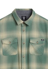Groene en beige geruite overhemd vervaardigd uit stof, met een button-down kraag, twee borstzakken en metalen knopen. Bevat een logolabel op de zak.