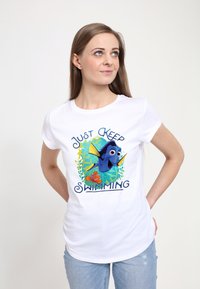 Bílý bavlněný tričko s barevným grafickým motivem modré ryby a oranžové klaunské ryby s frází "Jen pokračuj v plavání" v tučném písmu.