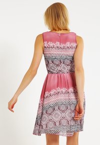 Ein ärmelloses pinkes Kleid mit einem Farbverlaufdesign und aufwendigen Schwarz-Weiß-Mustern, tailliert mit einem schwingenden Rock.