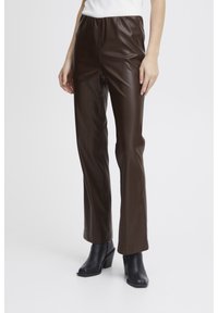 Pantalons en simili cuir marron avec une texture lisse, coupe ajustée et taille haute. Associés à des bottines noires à talons.