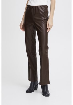 Pantaloni in similpelle marrone con una texture liscia, vestibilità slim e vita alta. Abbinati a stivaletti neri con tacco.