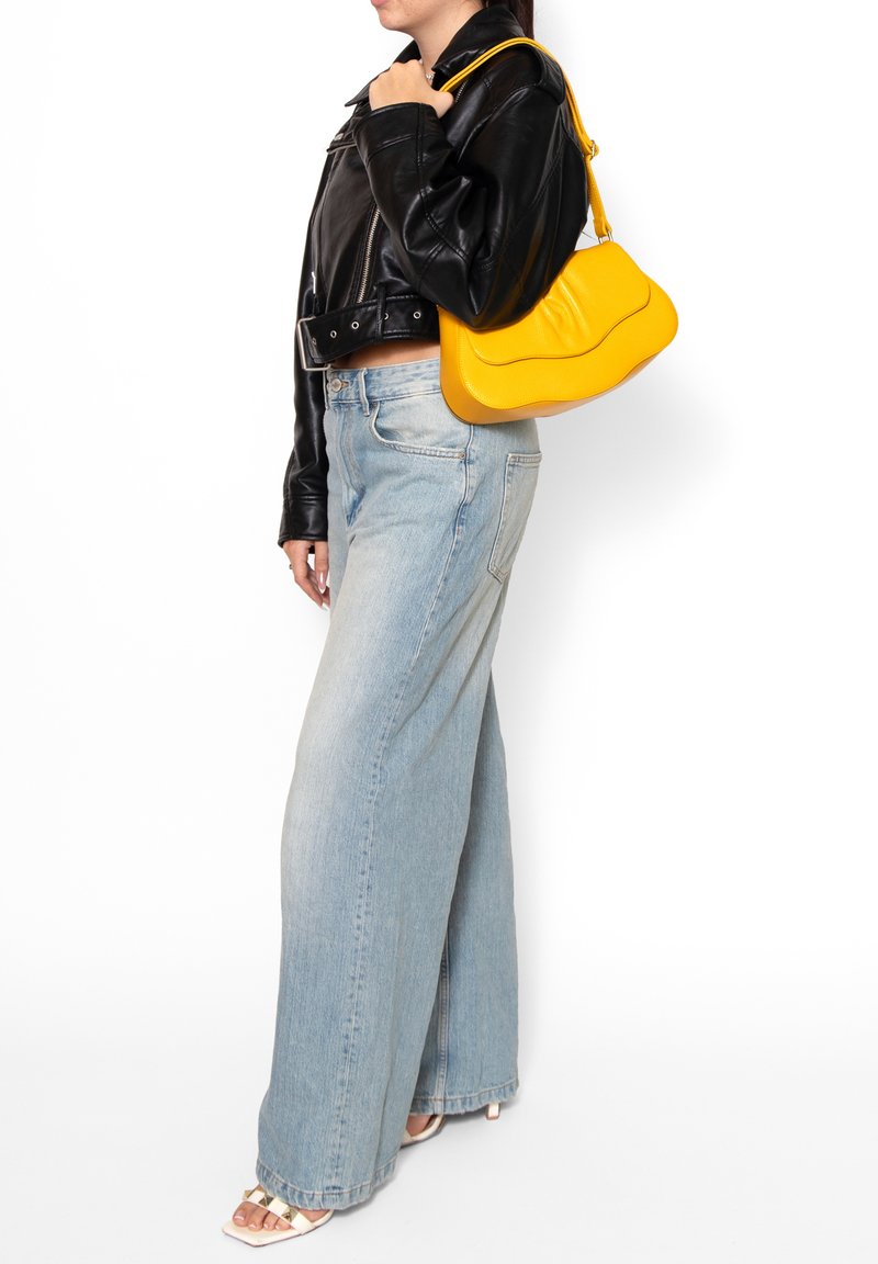 Geel leren handtas met een gebogen ontwerp, gecombineerd met een zwarte leren cropped jack en lichtgewassen wijde jeans.