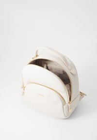 Hvit faux skinn ryggsekk med en avrundet design, gullfarget hardware, to glidelåslommer og et mønstrete interiørfor.