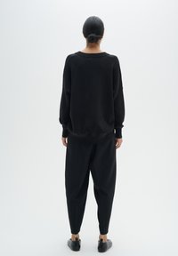 Black knit sweater with a relaxed fit, round neckline, and dropped shoulders; paired with tapered black trousers and flat shoes.