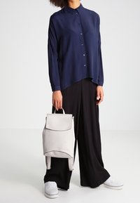 Marinblå skjorta med krage, matchad med lösa svarta byxor. Grå ryggsäck med en strömlinjeformad design. Vita sneakers fulländar looken.