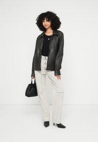 Črna usnjena jakna, črno zgornji del, svetle ohlapne jeans hlače, črna torbica in koničasti čeveljci. Preprost dizajn, gladka tekstura in nevtralne barve.