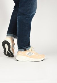 Light peach athletic shoes with a mesh and suede upper, featuring a gray logo, white midsole, and black outsole for traction.