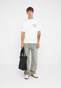 Witte katoen T-shirt met "Rock me, baby" in het zwart geborduurd, gecombineerd met vervaagde blauwe spijkerbroeken en een zwarte schoudertas. Schoenen met een bruine zool.