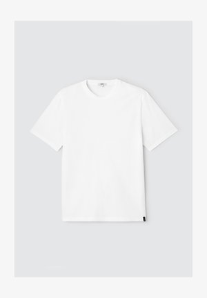 T-shirt blanc à manches courtes en coton, avec un col rond et une petite étiquette noire en bas à gauche. Design simple et uni.
