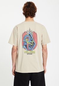 Beige cotton t-shirt featuring a colorful dragon graphic with red wings and blue accents, placed inside a diamond shape with a flame design.