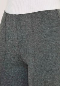 Nahaufnahme von grauen, strukturierten Hosen, die mit einem weißen, gerippten Oberteil getragen werden, und die Details des Stoffes sowie die Naht des Taillenbundes zeigen.