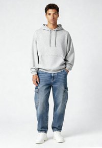 Pilkas gobtuvu megztinis su priekiu kišene, derinamas su laisvos talpos mėlynomis cargo kelnėmis, turinčiomis šonines kišenes. Balti sportbačiai užbaigia šį įvaizdį.