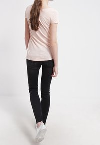 Světle růžová košile s krátkým rukávem spárovaná s černými skinny džíny a bílými teniskami. Měkká textura s přiléhavým střihem.