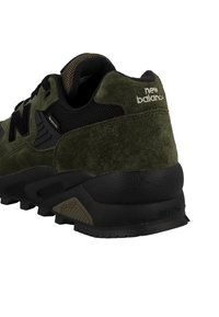 Zapatilla de ante verde con detalles de malla negra, suela de goma texturizada y prominente logo "N". En la parte trasera incluye el logo y un detalle "ROLLBAR" en negro.