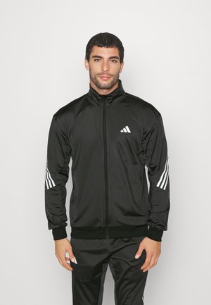 Veste de sport noire avec un col montant et une fermeture éclair complète. Présente le logo Adidas blanc et trois rayures blanches sur chaque manche. Texture lisse.