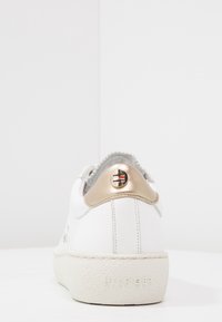 Vit läder sneakers med en strukturerad grå hälflik och glänsande gyllene detaljer. Har varumärke på hälen och en strukturerad vit sula.