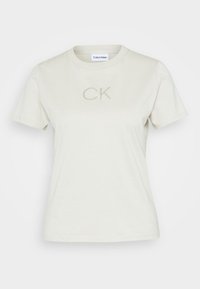 T-shirt in cotone a maniche corte con scollo rotondo di colore beige chiaro, dotato di un discreto logo "CK" in rilievo sul petto. Vestibilità rilassata.