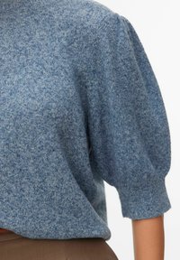 Jasnoniebieski dziany sweter z bufkami, ozdobiony teksturowanym wzorem i ściągaczami na mankietach. Stylizowany z taupe spodnie.