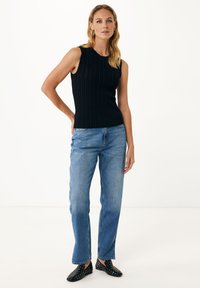 Černý bezrukávový žebrovaný top s kulatým výstřihem, v kombinaci se světle modrými rovnými džínami a černými botami na slip-on s bílými puntíky.