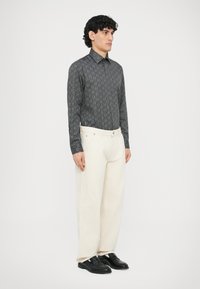 Czarna koszula z wzorem i długim rękawem, kremowe spodnie o szerokich nogawkach, czarne mokasyny. Gładki materiał, kołnierzyk na guziki, prosty krój i widoczne przeszycia.