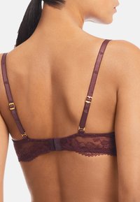 Burgunderfärgad spetsbh med justerbara satinförsedda axelband, med guldiga detaljer och en vågig spetskant bak.