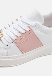 Weiße Leder-Sneaker mit pinkem Paneel-Akzent, mit strukturierten Oberflächen, weißen Schnürsenkeln und eingeprägtem Markenlogo an der Seite. Gummisohle.