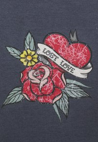 Cuore rosso con un banner che dice "Amore Perduto", circondato da rose rosa e foglie verdi, su uno sfondo di tessuto blu navy testurizzato.