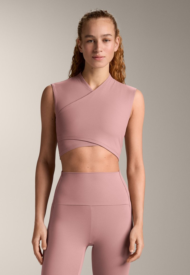 Light pink, cropped athletic top with a wrap design and ribbed texture. Paired with matching high-waisted leggings in the same material.