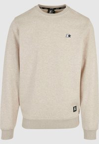 Sudadera de color beige claro, cuello redondo, con puños y dobladillo acanalados, que presenta un pequeño logo negro en el pecho y una etiqueta de marca en el lateral.