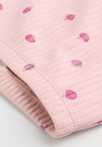 Tissu côtelé rose avec de petits motifs de cerises rose foncé, avec un bord plié et des coutures visibles.