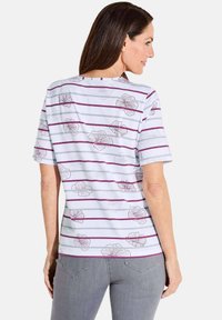 White t-shirt with purple horizontal stripes, featuring floral outlines. Short sleeves and a round neckline. Soft fabric texture.