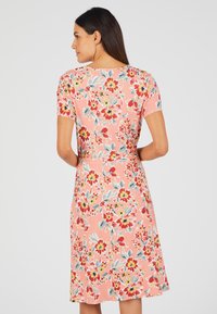 Vestido floral en coral con mangas cortas, que presenta un vibrante patrón de flores rojas, amarillas y azules, y un diseño de cintura ceñida.