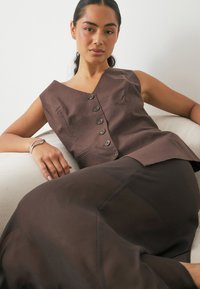 Top en lin marron avec un décolleté en V et des détails de boutons, associé à une jupe transparente marron. Texture de tissu lisse, coupe moderne.