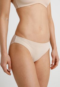 Beige seamless bikini panties featuring smooth fabric, subtle mesh detailing on the sides, and a classic cut for comfort.