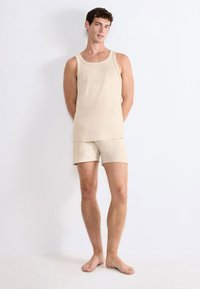 Beżowy komplet z topem na ramiączkach i szortami, wykonany z miękkiego materiału. Top ma okrągły dekolt i szerokie ramiączka; szorty mają elastyczny pas.
