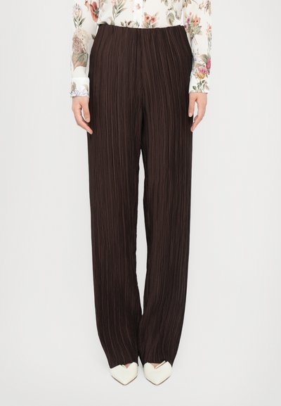 Pantalons amples plissés marron en tissu texturé. Dotés d'une taille élastique et d'une coupe loose, associés à des chaussures blanches à bout pointu.