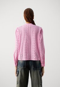 Blusa lunga rosa a maniche lunghe con motivo a occhio di pernice, tessuto testurizzato e maniche arricciate, abbinata a pantaloni in denim larghi.