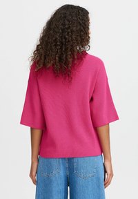 Pull rose côtelé avec une coupe ample, des manches courtes larges et un col rond, associé à un jean bleu taille haute à jambes larges.