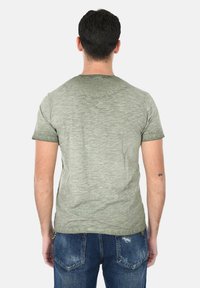 T-shirt in cotone verde melangiato con collo a giro, maniche corte e vestibilità morbida, abbinato a jeans in denim blu.