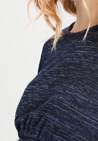 Mörkblå texturerad topp med rundad halsringning, korta ärmar och samlad detalj vid midjan. Mjukt, lättviktigt tyg.