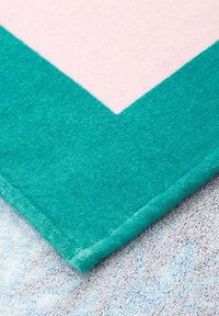 Tapis de bain rectangulaire en teal et rose clair, présentant une surface douce et texturée avec un motif en zigzag le long des bords.