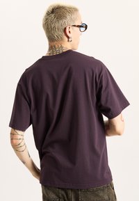 Purple unisex crew neck t-shirt made of cotton, featuring short sleeves and a relaxed fit, shown from the back with visible stitching details.